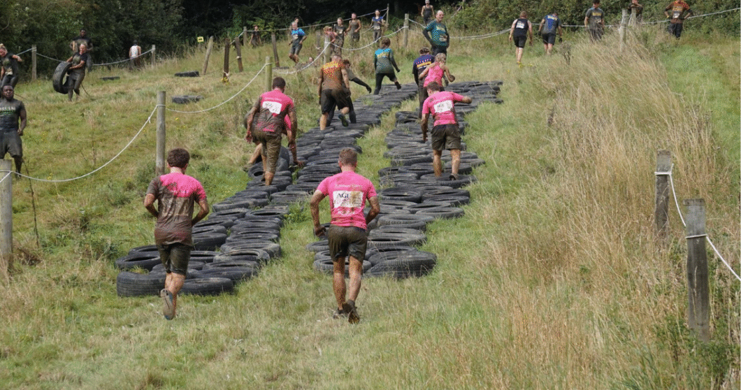 Fundraisers climb a tire wall as part of a physical challenge.